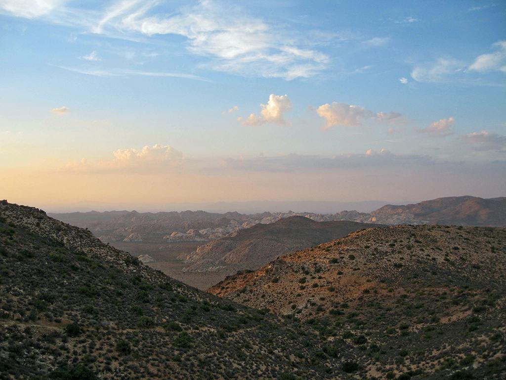 Sunlight and clouds in a blue sky over an expansive desert mountain landscape, Joshua Tree National Park