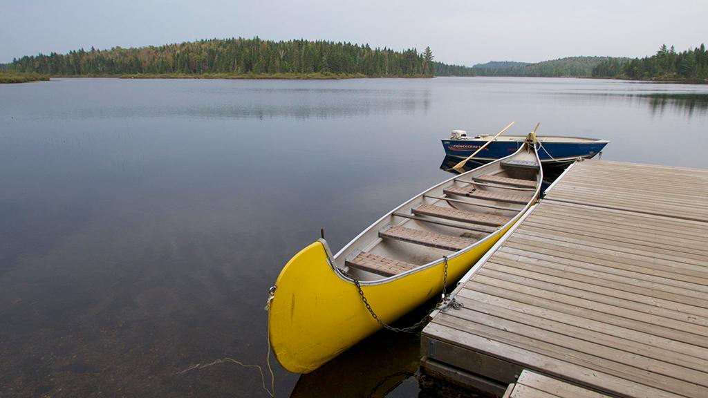 A yellow canoe and blue motorboat next to a dock on a still lake, La Mauricie National Park