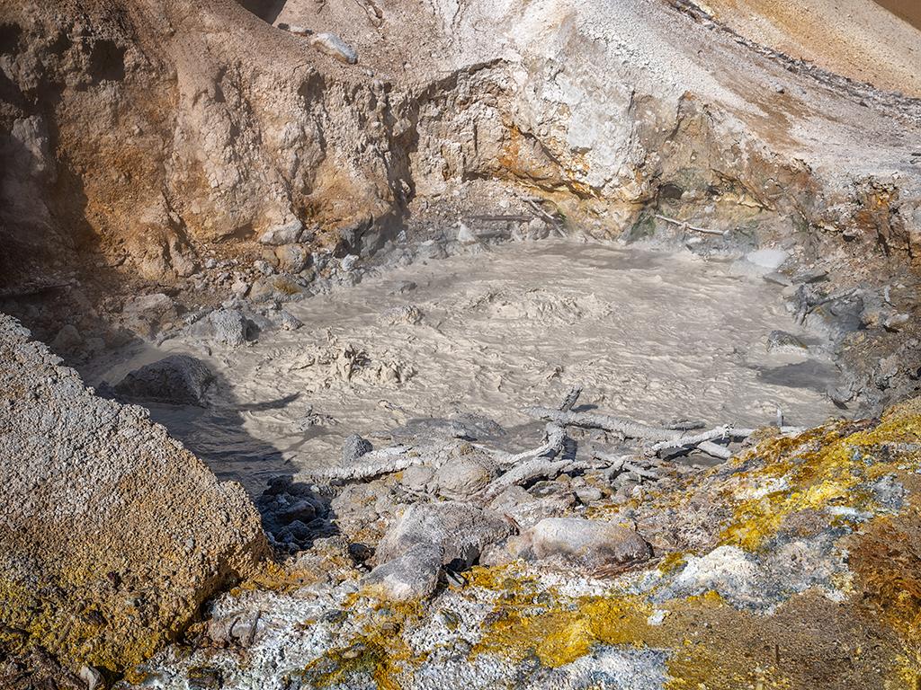 A depression filled with bubbling brown water rimmed by similar colored rocks at Sulphur Works, Lassen Volcanic National Park, California