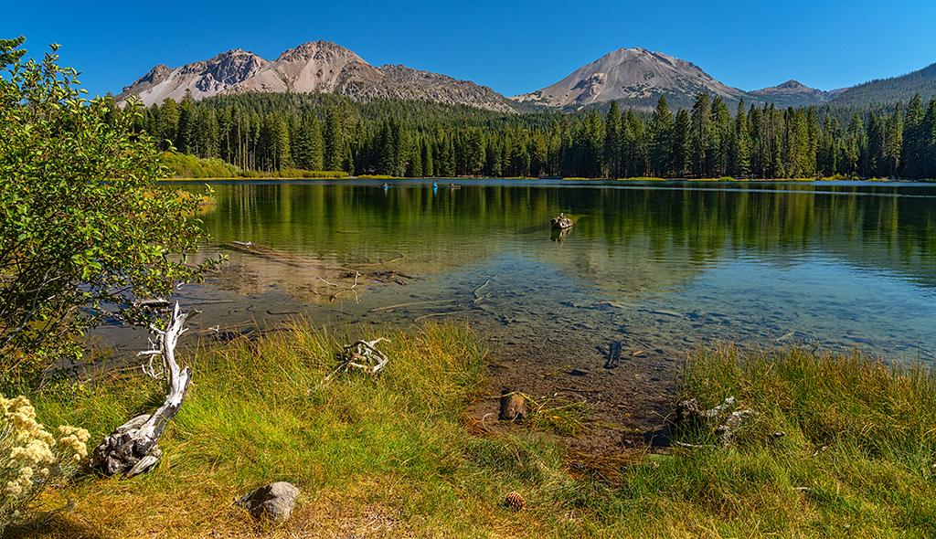 A bright, clear autumn afternoon with blue sky at a calm Manzanita Lake with Chaos Crags and Lassen Peak towering over the scene, Lassen Volcanic National Park