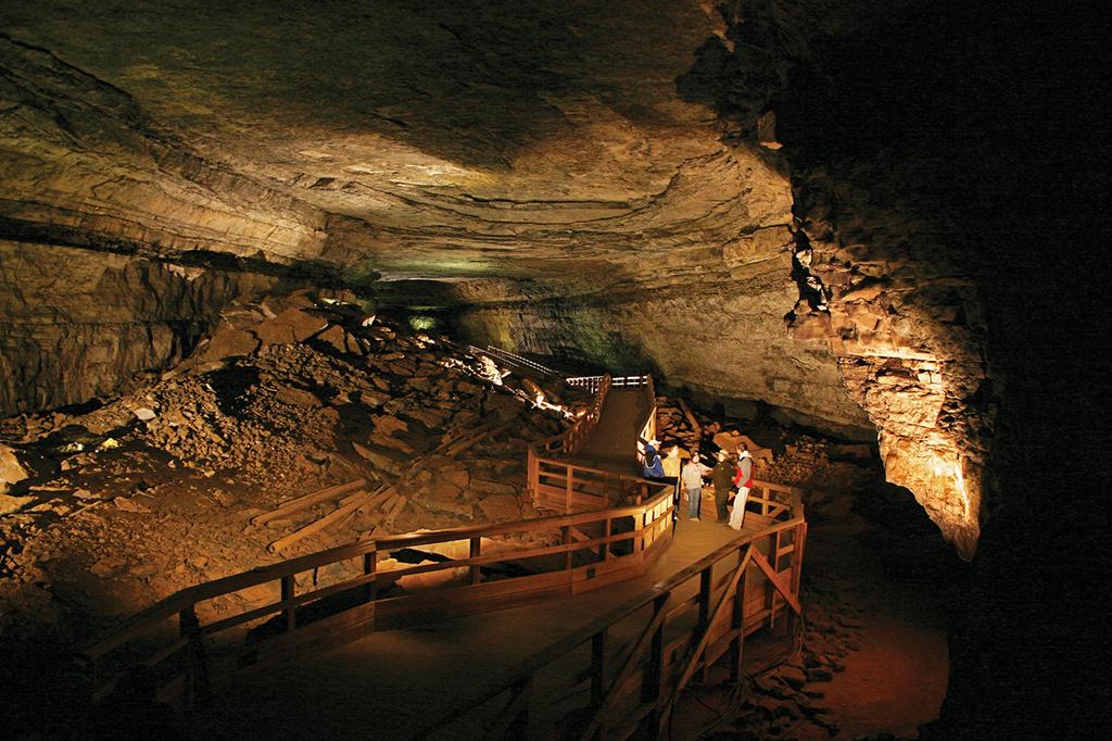 a large cave room lit up to show a boardwalk running through the middle of it with a group of people walking along it in Mammoth Cave National Park