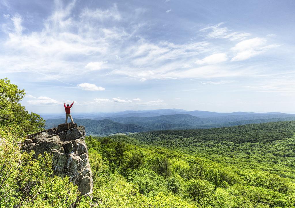 A person with upraised arms standing on a rock outcrop viewing the vast scenery of Shenandoah National Park