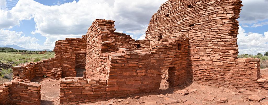 A red sandstone pueblo with one large wall and the remains of several rooms at Wupatki National Monument.