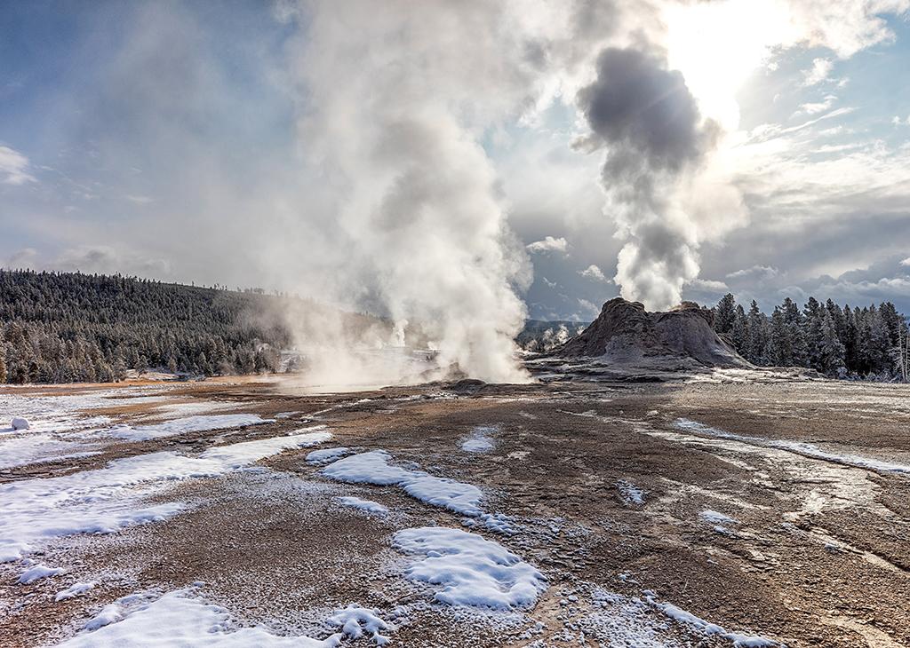 A steaming Castle Geyser backlit by the morning sun at Upper Geyser Basin in Yellowstone National Park