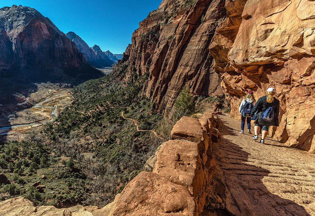 A wide-angle shot of hikers heading down the Angels Landing Trail in Zion National Park, Utah