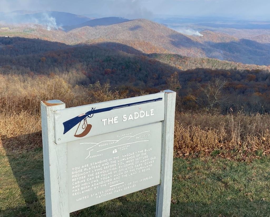 Looking beyond an interpretive sign at milepost 168 on the Blue Ridge Parkway, smoke from the Tuggle’s Gap fire is seen in the distance/NPS