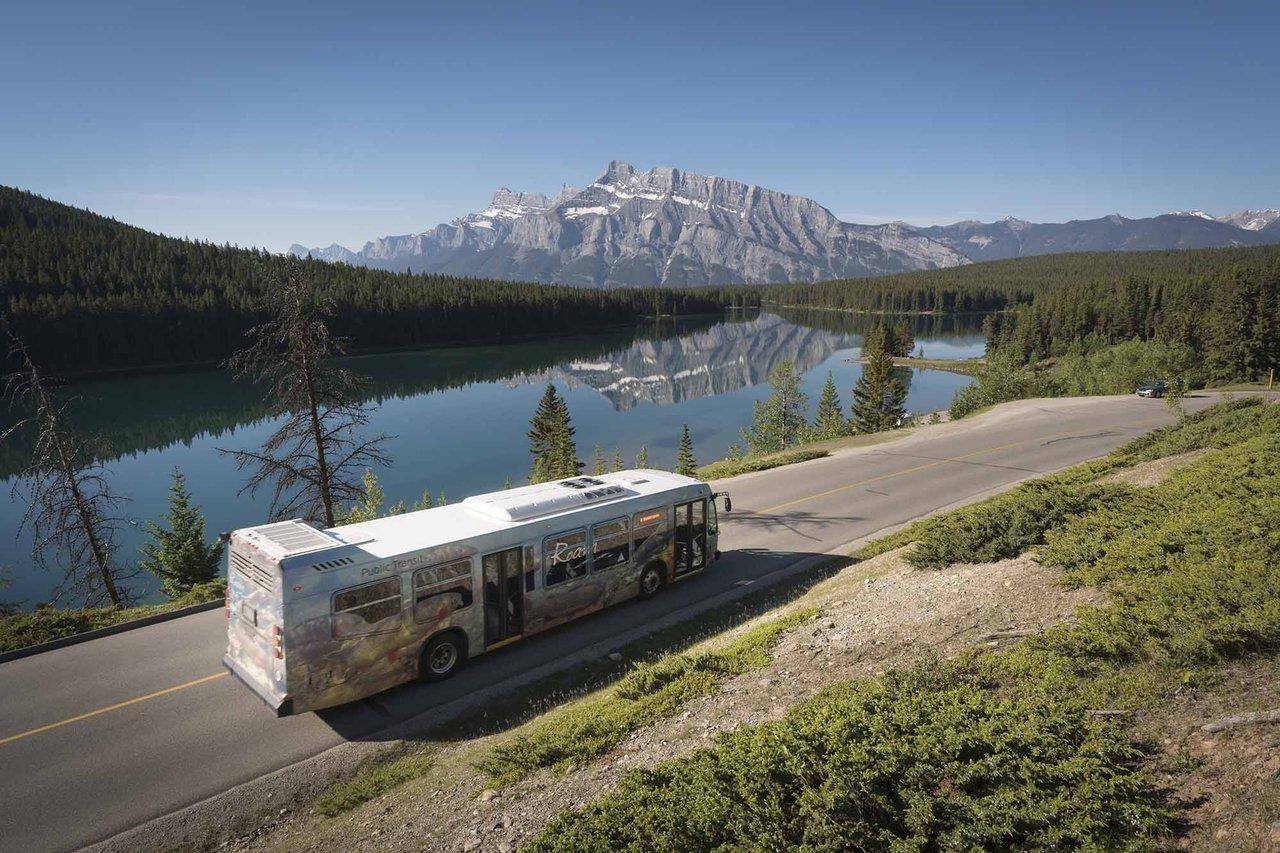 A Roam Public Transit bus is shown passing Two Jack Lake and Mount Rundle in Banff National Park.