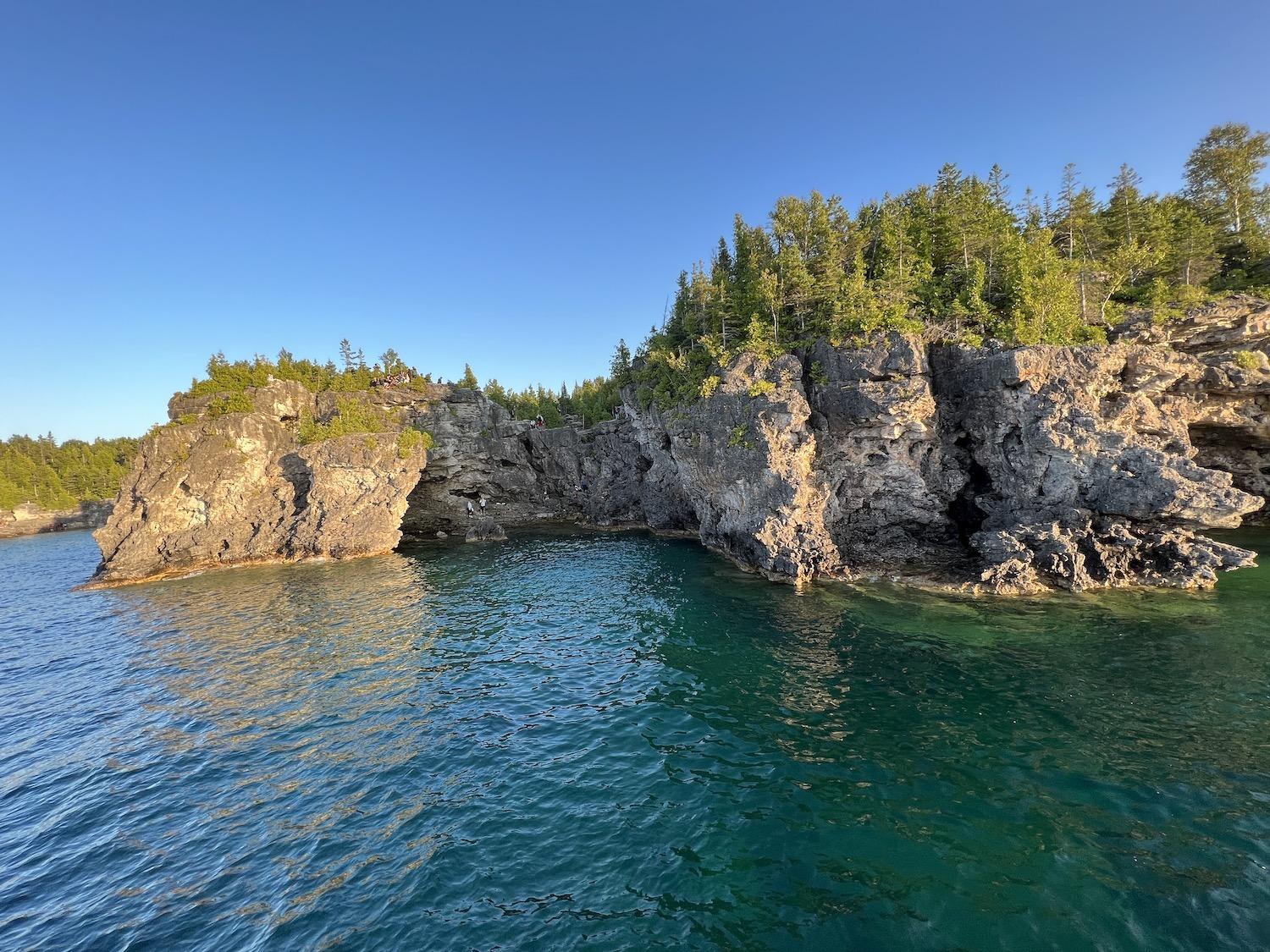 A view of people exploring the Grotto, taken from a sunset cruise along Georgian Bay.