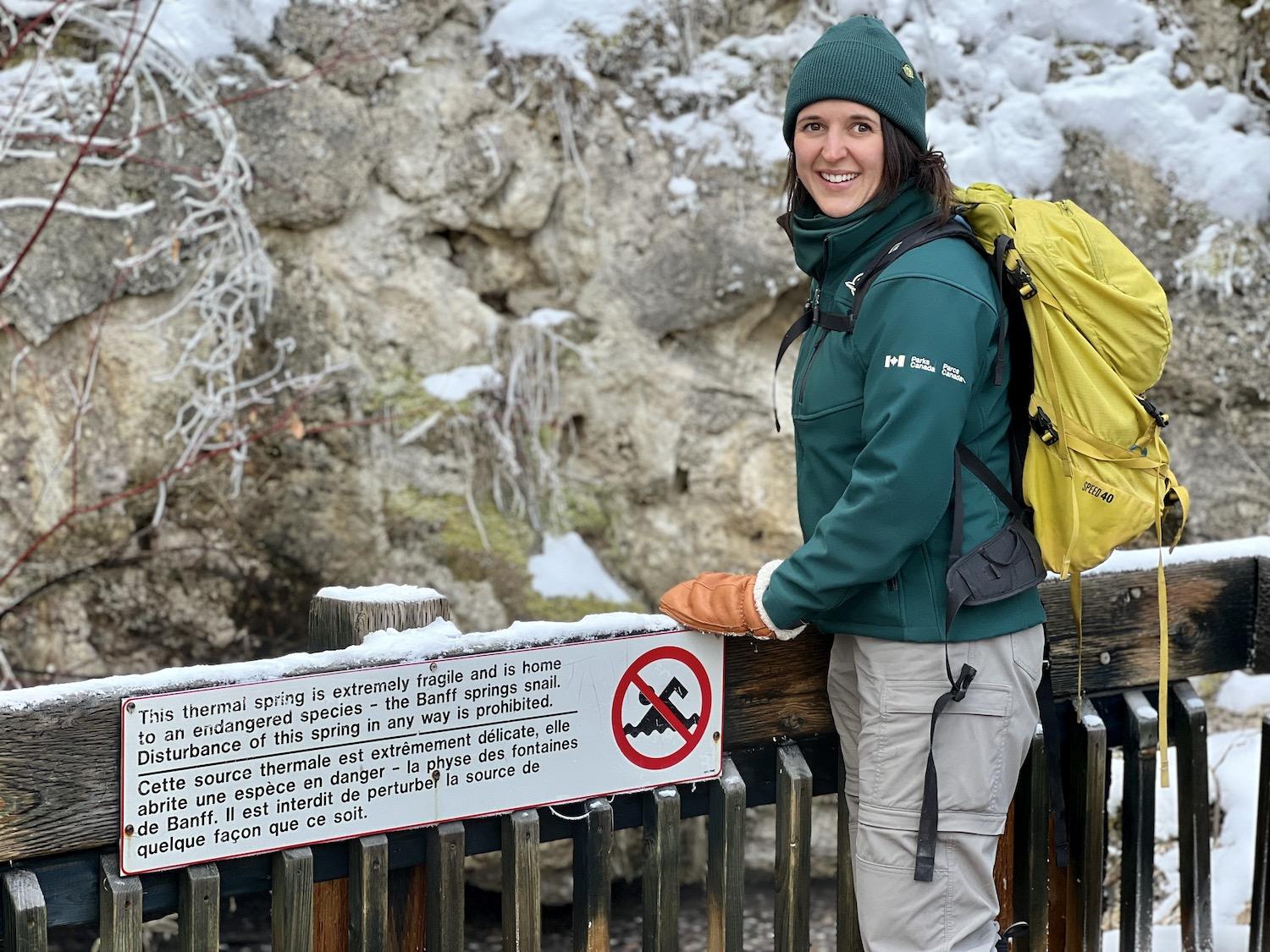 Resource conservation officer Kate Keenan stands by a warning sign that protects endangered Banff Springs Snails in Cave and Basin National Historic Site.