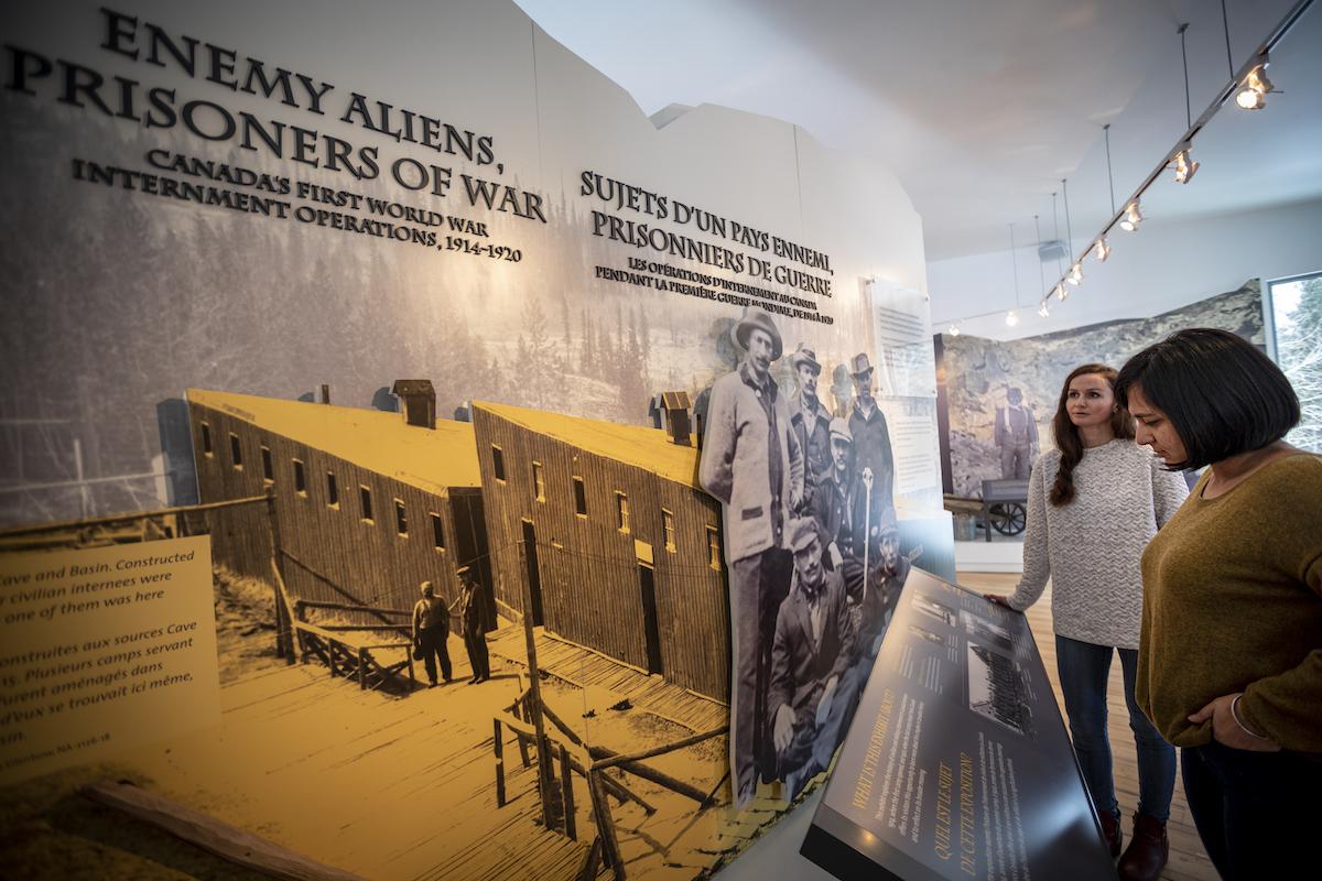 Visitors read the "Enemy Aliens, Prisoners of War" internment diorama at Cave and Basin National Historic Site.