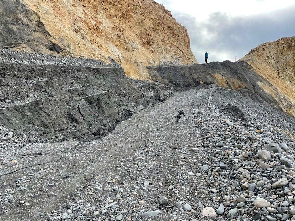 September 16, 2021 photo of eastern side of the Pretty Rocks landslide. The displacement of approximately 14 vertical feet seen below the person standing on the stable road surface (for scale) occurred over two weeks following the cessation of maintenance