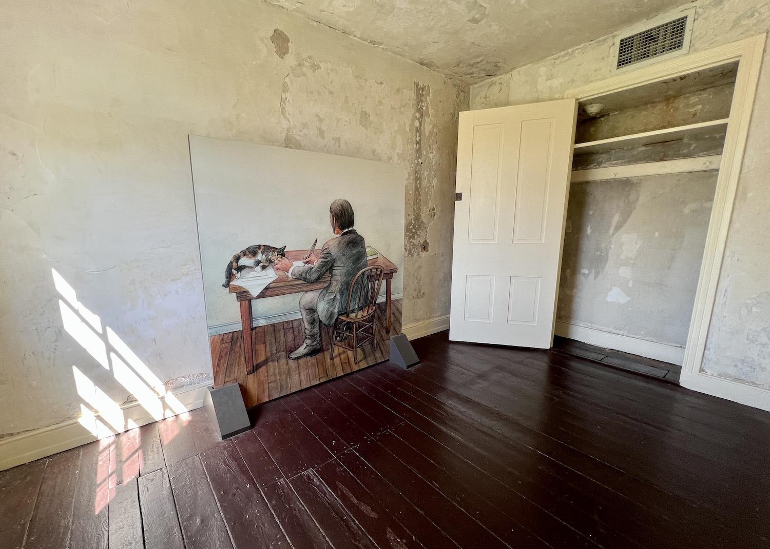 In a small second-floor room, a painting depicts Edgar Allan Poe writing alongside his cat.