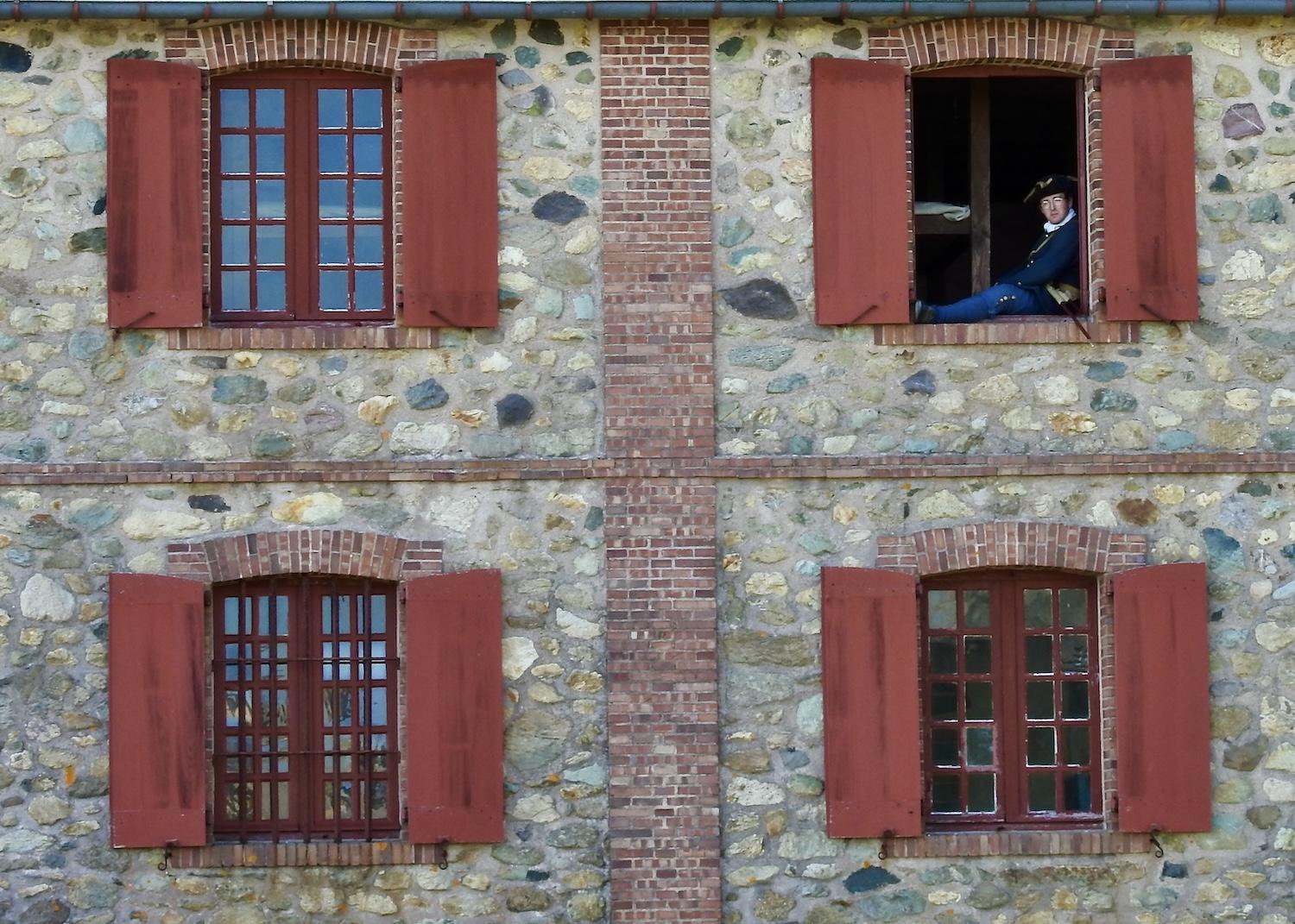 A costumed interpreter is seen resting in a window at the Fortress of Louisbourg National Historic Site.