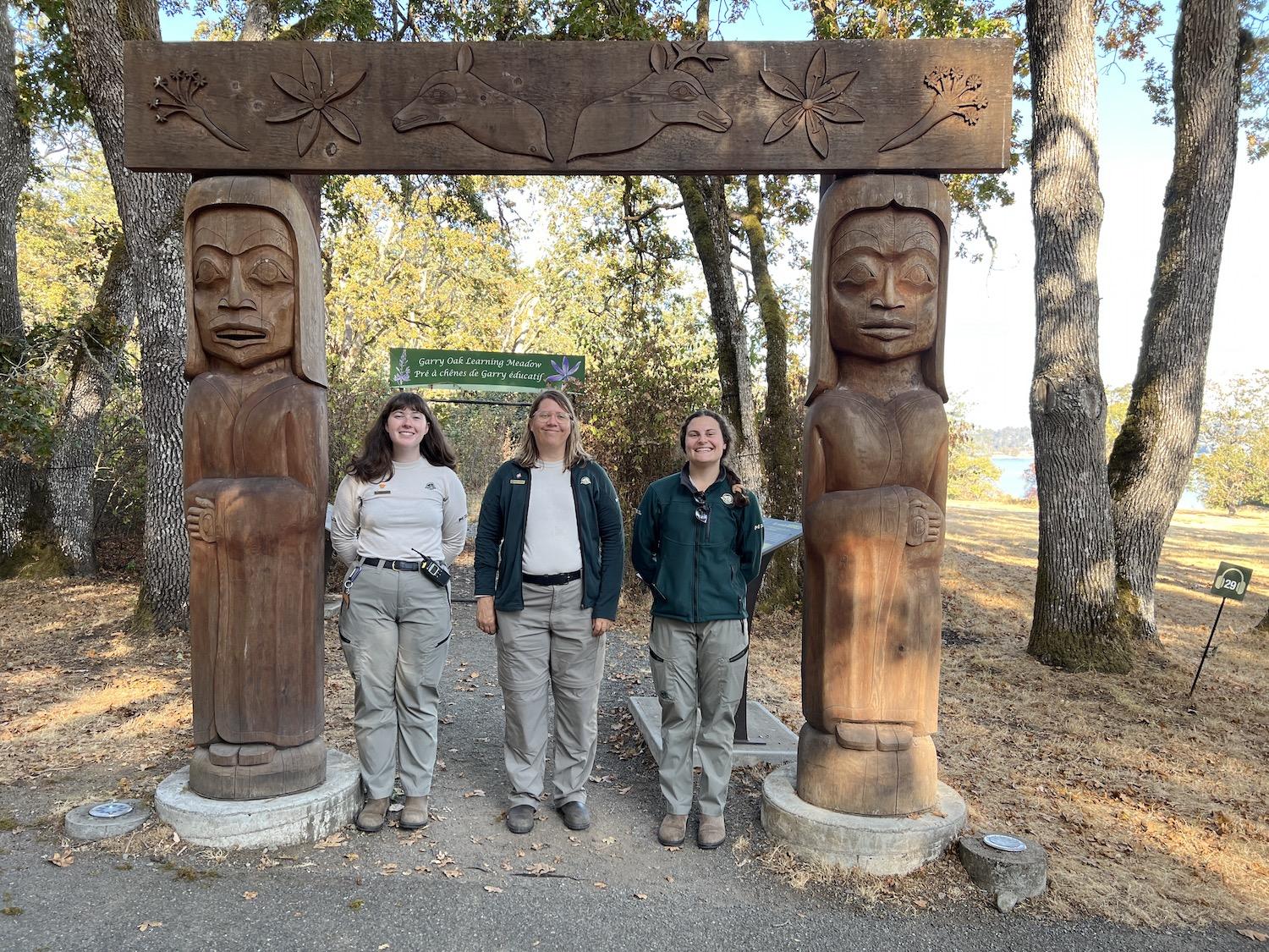 At the entrance to the Garry Oak Learning Meadow, Parks Canada's Anna Lee, Aimée Pelletier and Ashley Everitt stand under the welcome arch carved by Tom LaFortune.