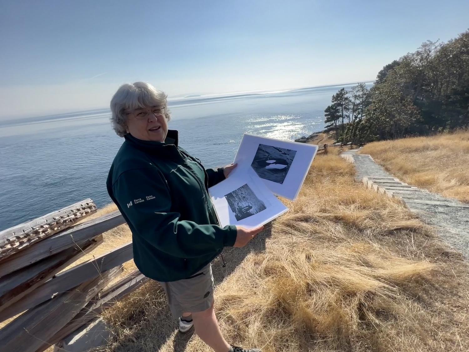 Parks Canada's Athena George stands just above the spot where Moby Doll was harpooned in 1964, and holds archival photos of the killer whale.
