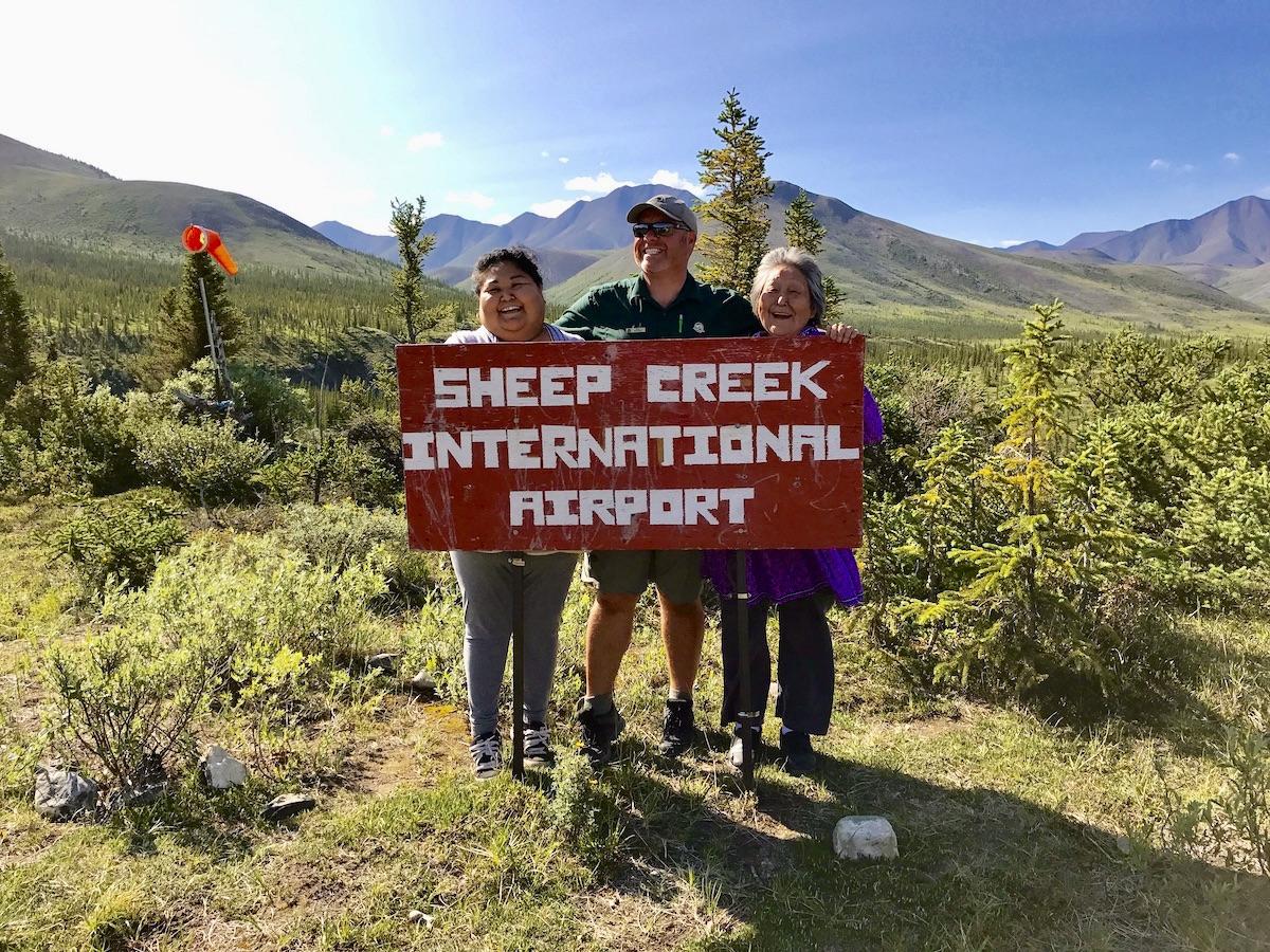 A trio of Ivvavik National Park staff at the Sheep Creek International Airport sign.