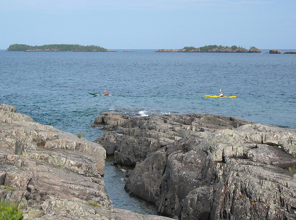 A rocky shoreline with kayakers, Isle Royale National Park / National Park Service