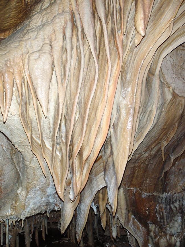 Cave drapery speleothem created when calcium carbonate-laden water flows down a sloped ceiling, depositing the calcium before dropping to the floor, Jewel Cave National Monument / NPS Cave drapery speleothem created when calcium carbonate-laden water flows down a sloped ceiling, depositing the calcium before dropping to the floor, Jewel Cave National Monument / NPS