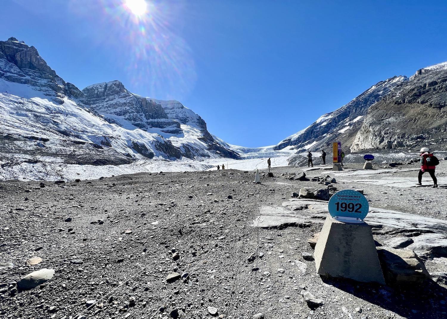 A small sign marks where the Athabasca Glacier was in 1992, as visitors walk freely on the right and visitors with guides access a restricted area on the left.