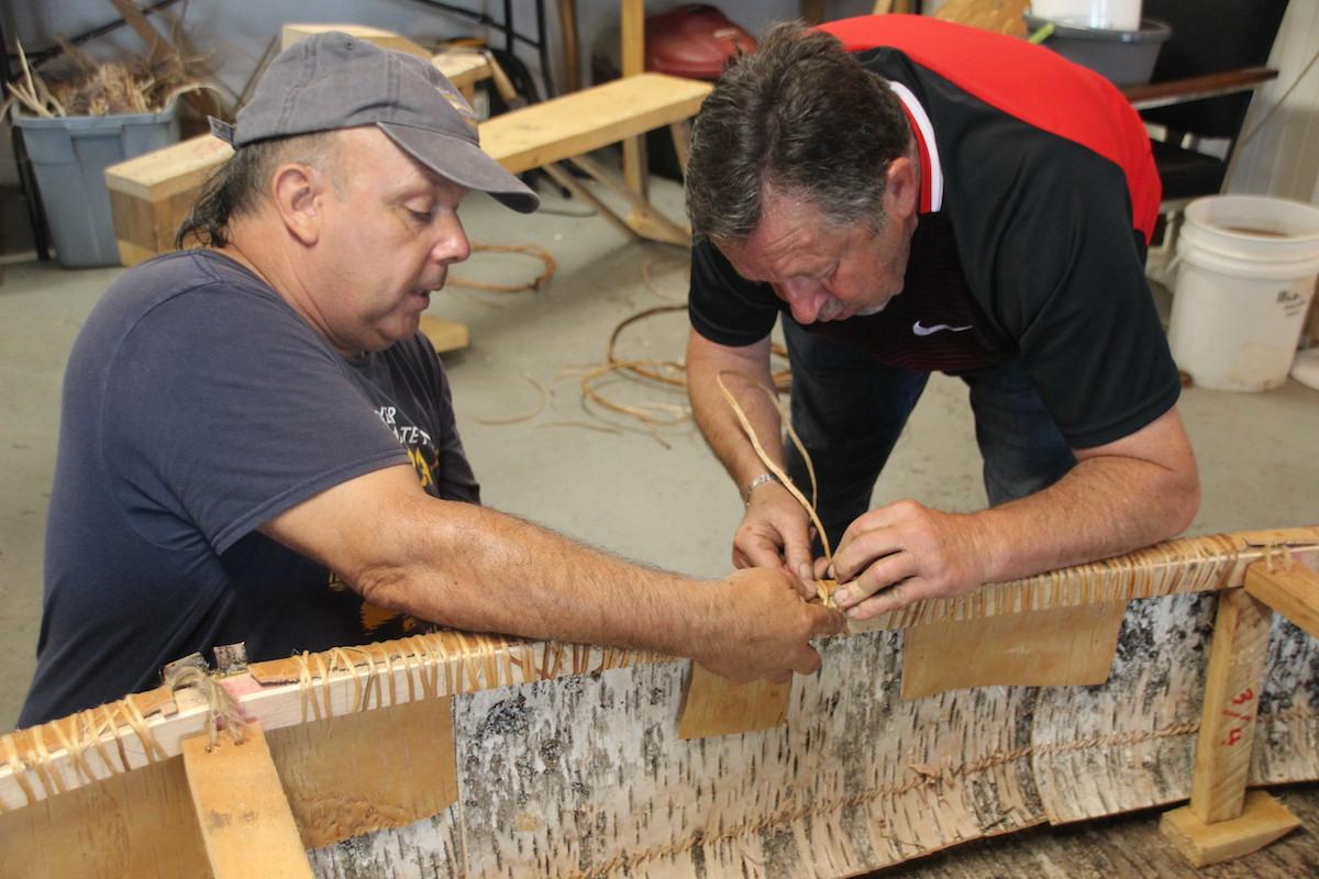 Todd Labrador, left, shows a workshop student how to secure birch bark to the canoe frame.
