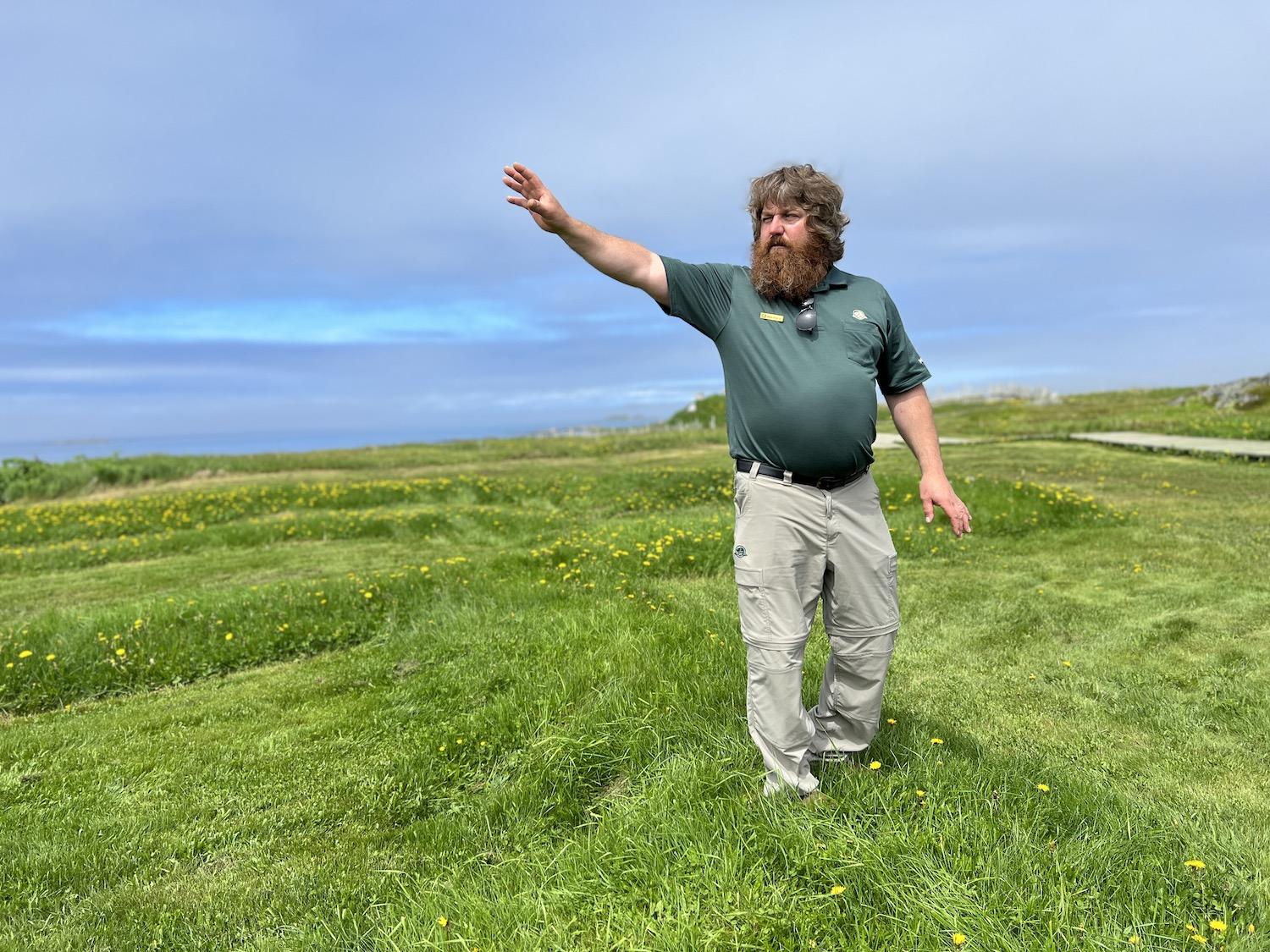 Heritage presenter Mark Pilgrim stands on grass above the remains of a Norse settlement from 1,000 years ago.