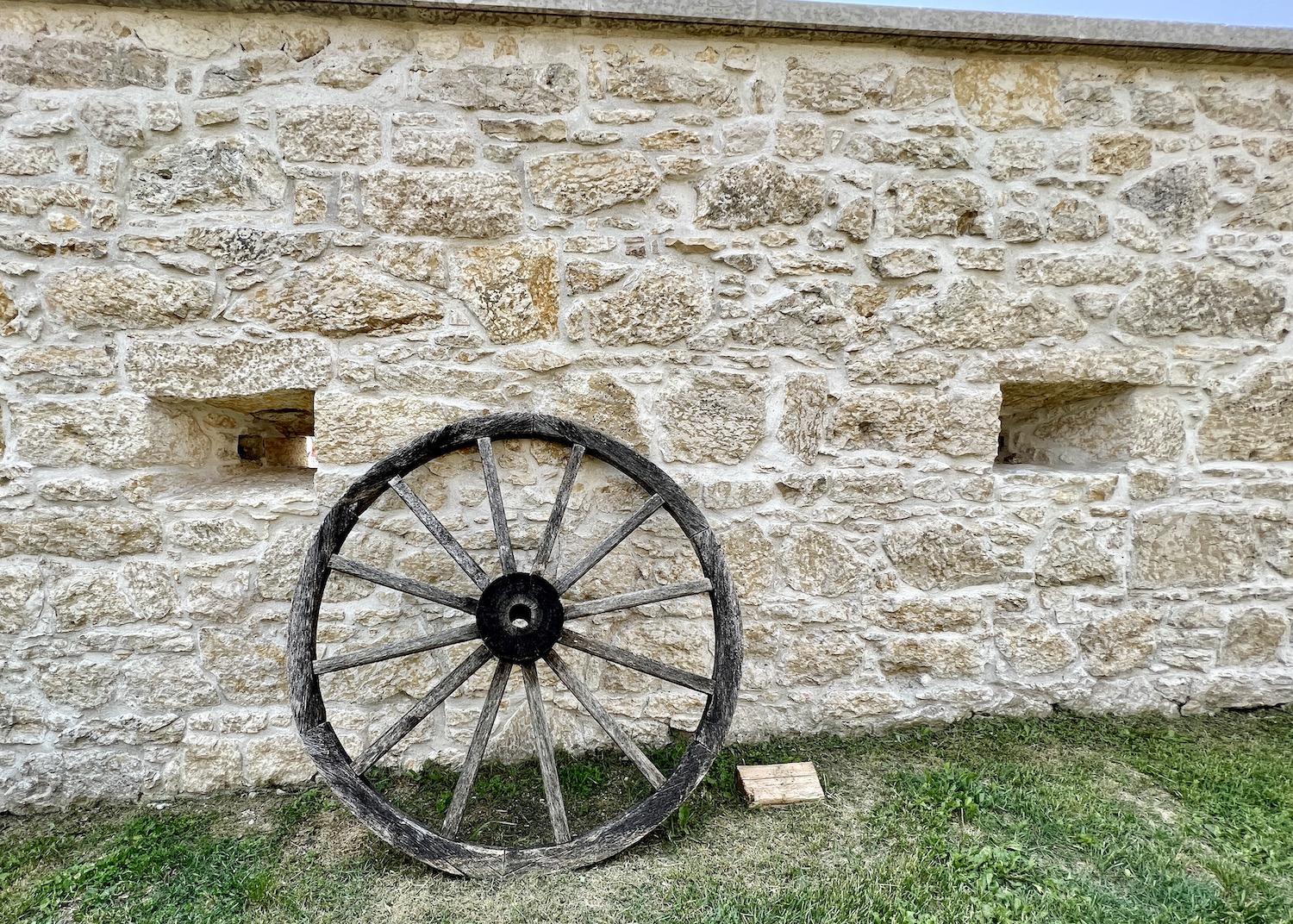 The wooden wheel of a Red River cart leans against a Tyndall Stone wall at Lower Fort Garry.