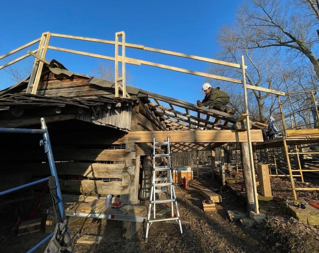 Worker in safety gear putting new roof on log barn. NPS / Schier