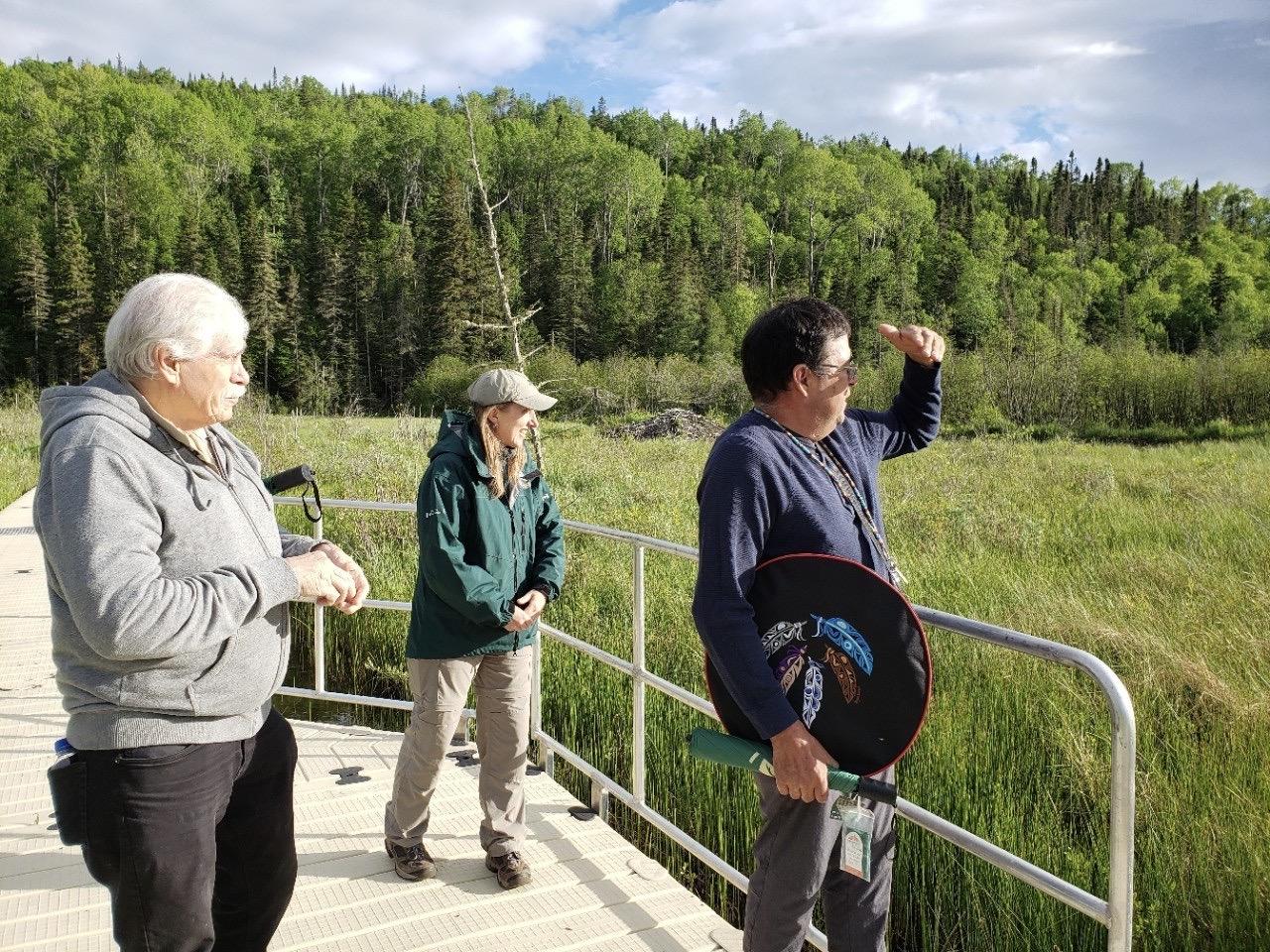 Biigtigong Nishnaabeg Chief Michano (left), Pukaskwa National Park’s park manager Christine Drake (center) and Knowledge Keeper Donald Michano (right) look out over Hattie Cove wetland from the recently replaced walkway.