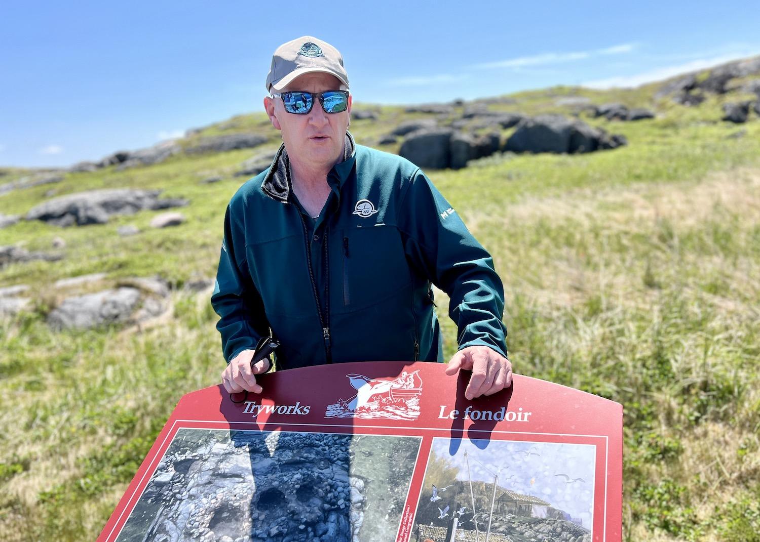 Heritage presenter Kirby Ryan stands on Saddle Island by signage about tryworks from the Basque whaling era in Labrador.