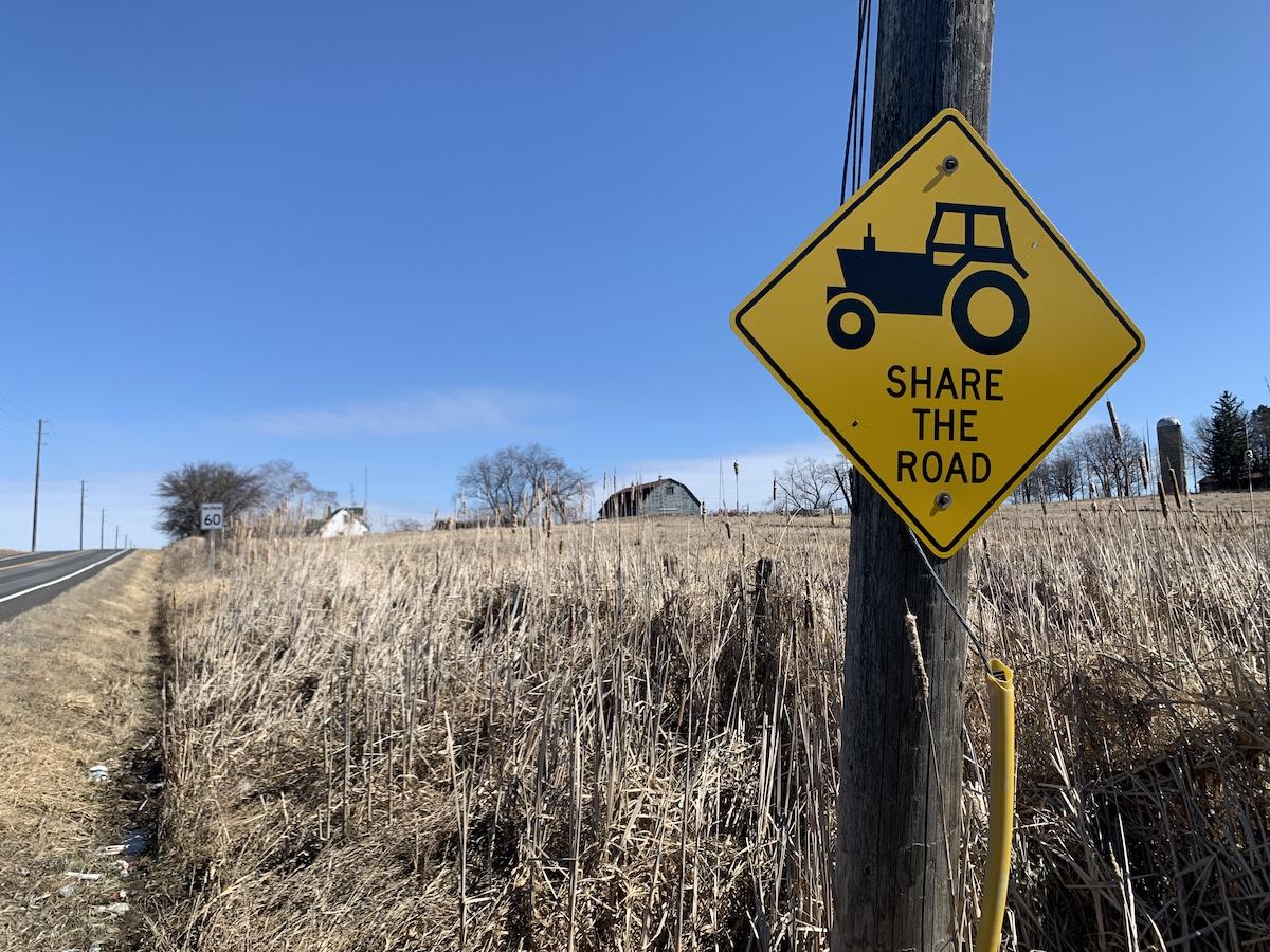 A sign says to share the road with tractors as a farm and barn loom in the background.