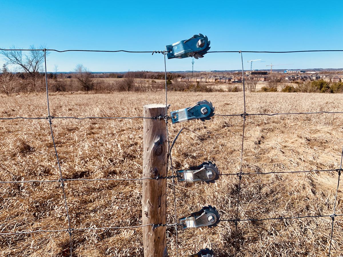 Fence strainers (wire tigheners) on a park fence by farmland.