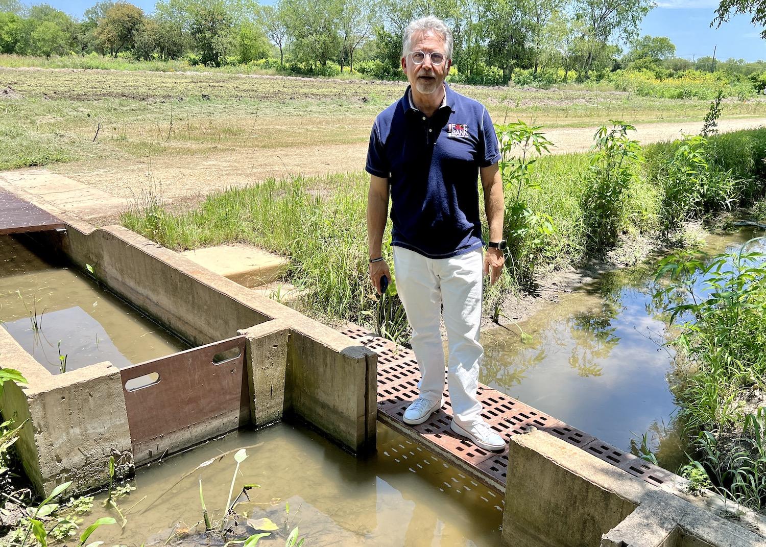 Michael G. Guerra, chief resource officer with the San Antonio Food Bank, stands over an acequia near the fields the food bank farms for food and for demonstration purposes.