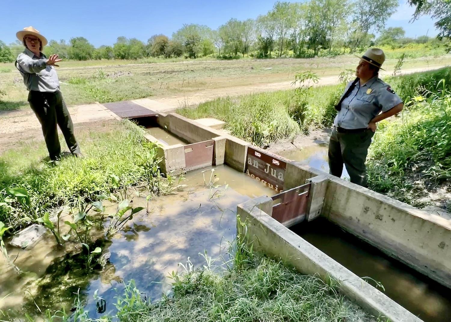 At Mission San Juan, Superintendent Christine Jacobs and Ranger Destiny Gardea stand at the sluice gates of an ancient acequia that is used to water fields farmed by the San Antonio Food Bank.