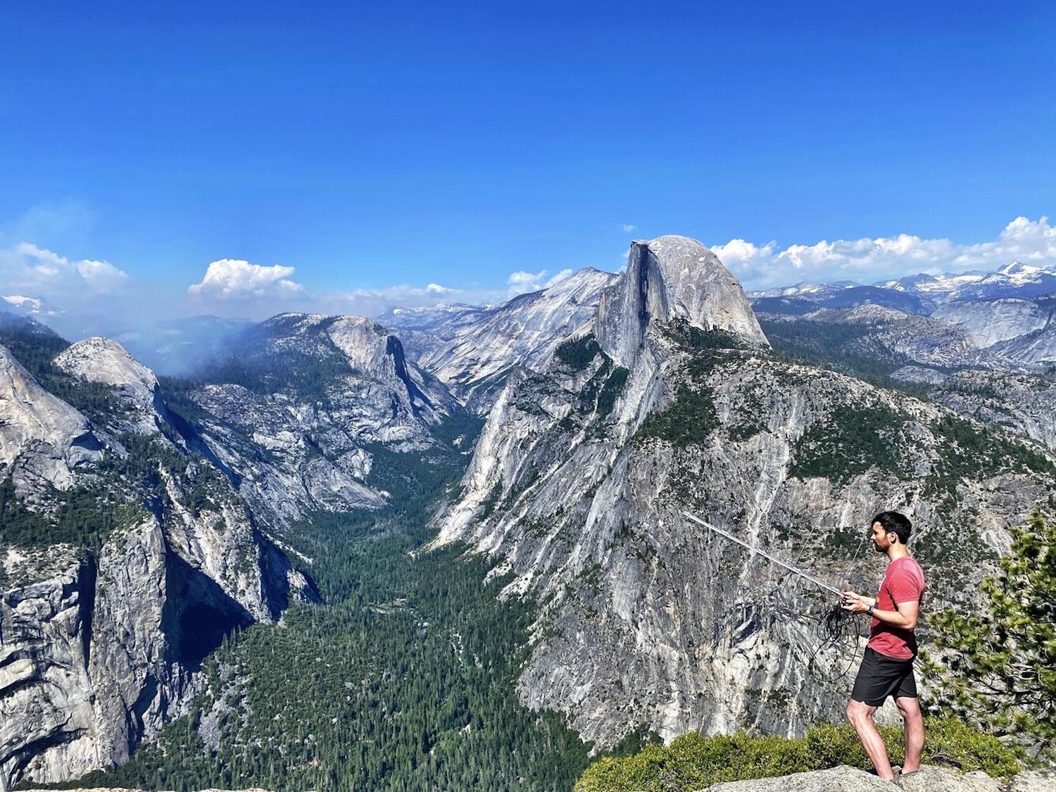 Austin Waag performing radio-telemetry at Glacier Point with Half Dome in the background, as part of a project tracking bats in Yosemite National Park.