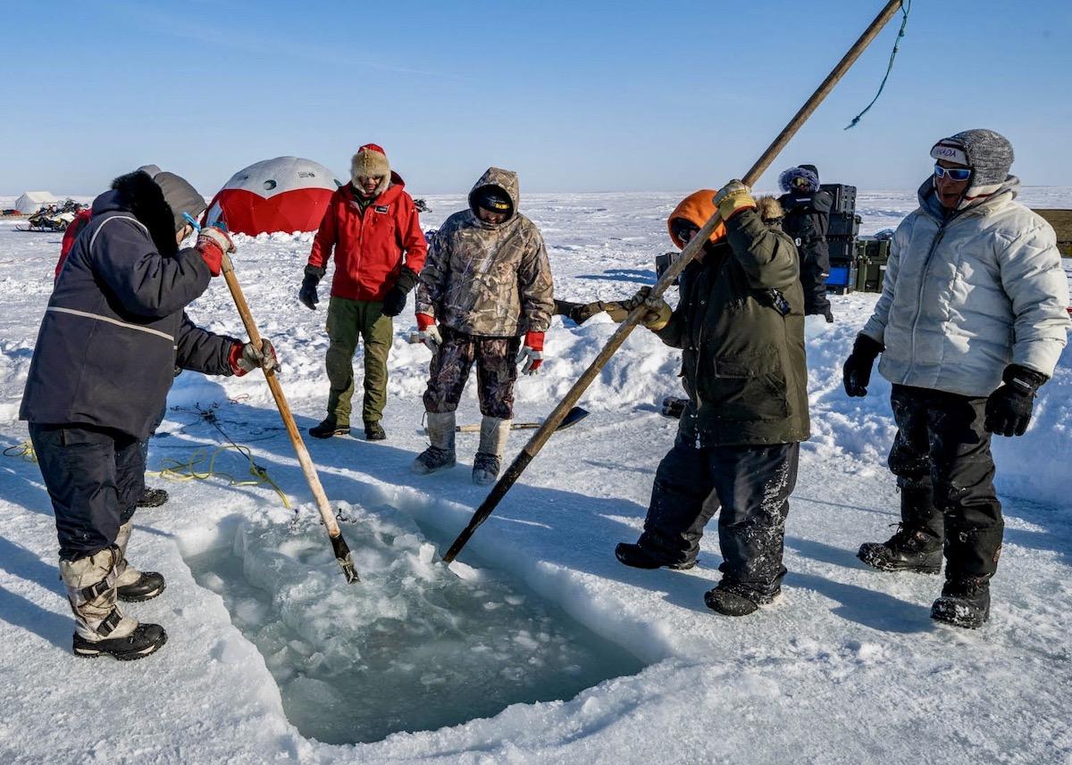 Inuit Guardians and Parks Canada underwater archaeology team members remove ice from the remotely-operated vehicle (ROV) hole at the HMS Erebus site in April 2022.