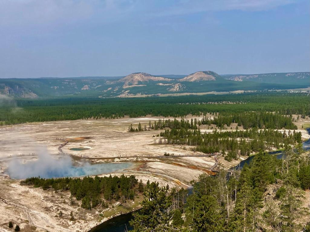 Photograph of Twin Buttes in Lower Geyser Basin looking to the northwest, with Excelsior Geyser of Midway Geyser Basin in the foreground. Twin Buttes is a thermal kame that formed when glaciers covered the area, and hydrothermal activity below the ice led