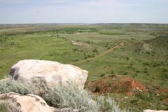 A white rock overlook with a view of green scrubland and red dirt at the Alibates Flint Quarries National Monument in Texas