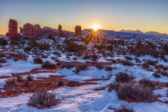 A sunstar rising above the horizon and shining over Balanced Rock and other red-rock sandstone formations within Arches National Park, Utah.