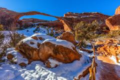 Snow and red rock around Landscape Arch with a frozen sand trail toward the arch in Arches National Park