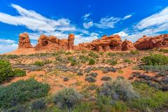 A line of red-rock arch formations with a blue sky and white clouds in the Windows Section of Arches National Park