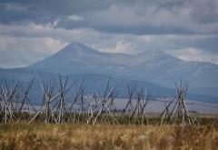 Tipi poles on a dry grass prairie with tall blue mountains in the distance and dramatic storm clouds overhead, Big Hole National Battlefield