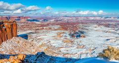 A sprinkling of snow over Buck Canyon and surrounding landscape beneath a blue sky with puffy clouds in the Island-in-the-Sky District of Canyonlands National Park