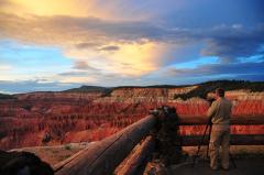 A photographer standing at a fenced view area overlooking the colorful Golden Hour of a part of Cedar Breaks National Monument