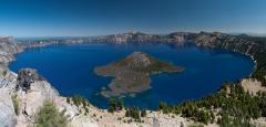 A wide-angle image of the entire width of Crater Lake on a sunny day with a clear sky in Crater Lake National Park
