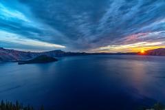 A sunburst sunrise climbing above the caldera rim and beginning to shine on Wizard Island in Crater Lake National Park