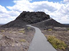 A small, black volcanic cone with a paved trail winding up and around the side, Craters of the Moon National Monument and Preserve