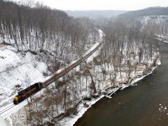The leading line of a train on train tracks over a snowy landscape with bare trees beneath a white sky, Cuyahoga Valley National Park