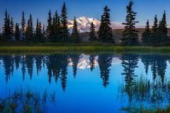 Sunrise over Denali Mountain against a blue sky reflecting in the blue water of Nugget Pond, Denali National Park and Preserve