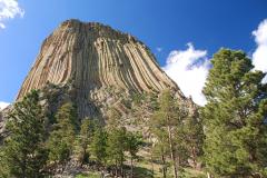 The towering columnar basalts of Devils Tower National Monument beneath a blue sky with fluffy clouds