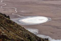 A telephoto image of an almost perfectly-round salt pan on the floor of Death Valley with a long, squiggly white line of salt connecting to the salt pan, Death Valley National Park